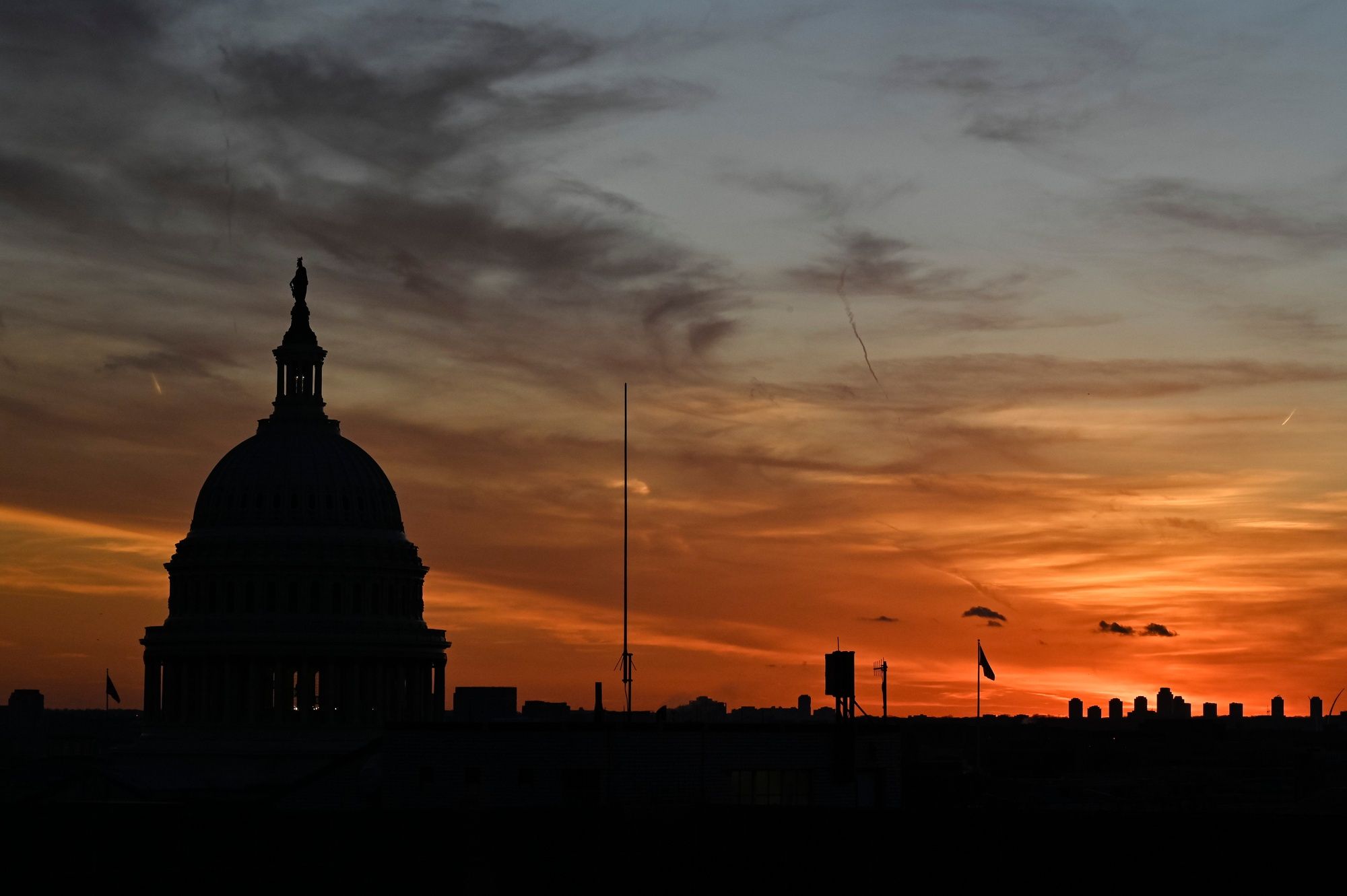 The dome of the U.S. Capitol in silhouette against an orange sunset sky.
