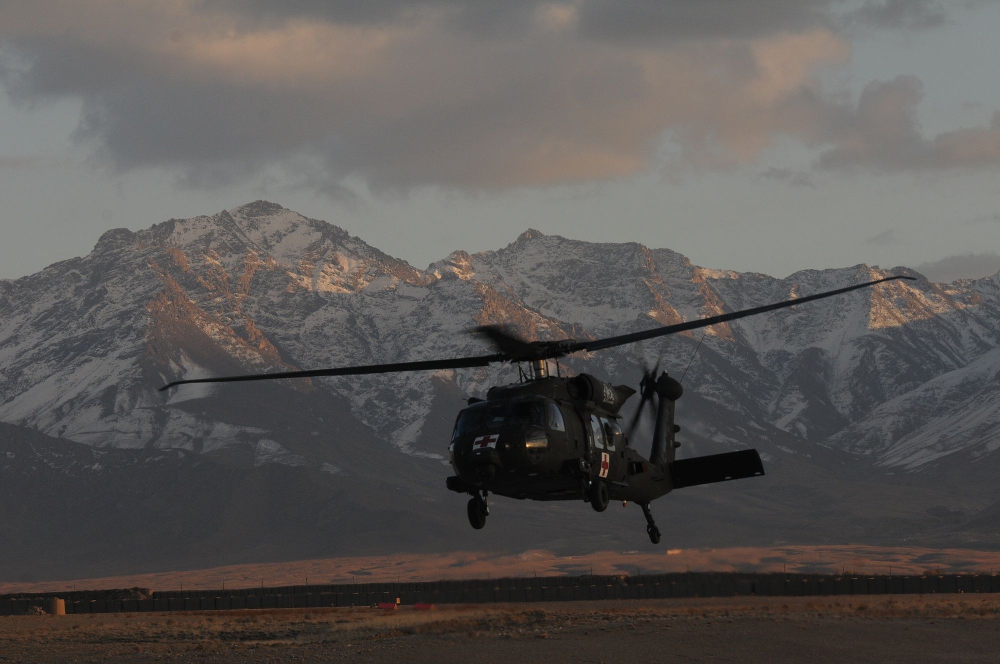 A medevac helicopter flies low in front of snow-capped mountains.